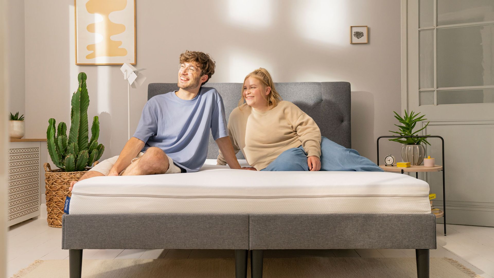 Junges Paar sitzt entspannt auf Emma Boxspringbett in sonnigem Zimmer.